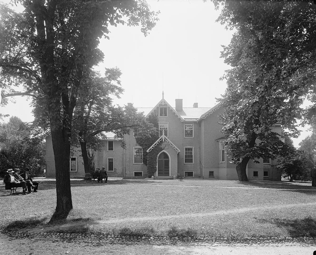Early 1900s photograph of the Cottage at the Soldiers’ Home, with veterans resting on benches beneath the trees